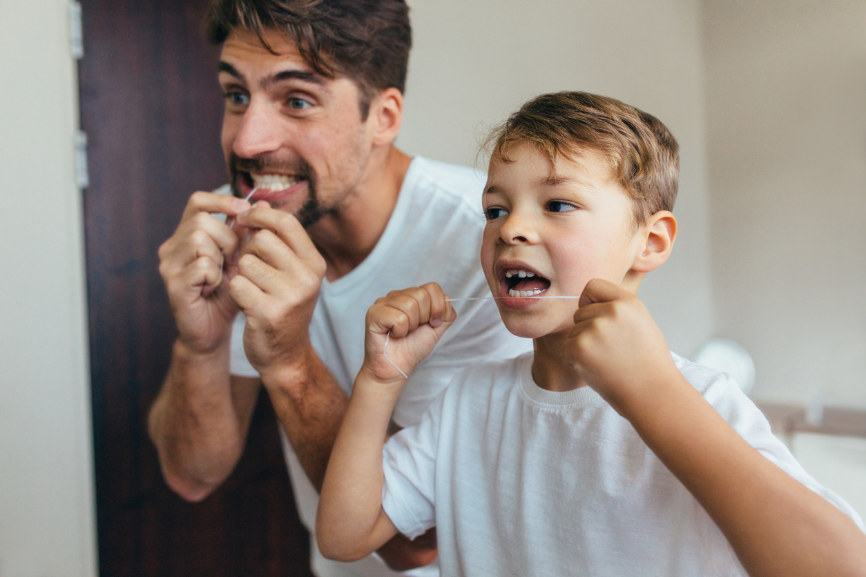 A parent teaching their child how to floss to prevent early-stage gum disease and gingivitis.