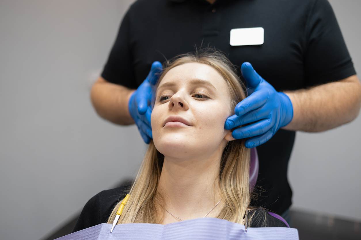 A dentist assessing a patient's jaw muscles for TMJ pain and therapeutic injectable treatment at Morrin Dental Newcastle